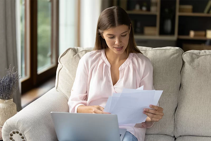 Woman in front of laptop with papers in hand.
